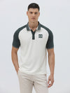 A man modeling a short-sleeve polo shirt with a white body and dark green raglan sleeves, featuring a striped collar and a small 'CR' logo on the chest, paired with beige trousers against a light gray background.