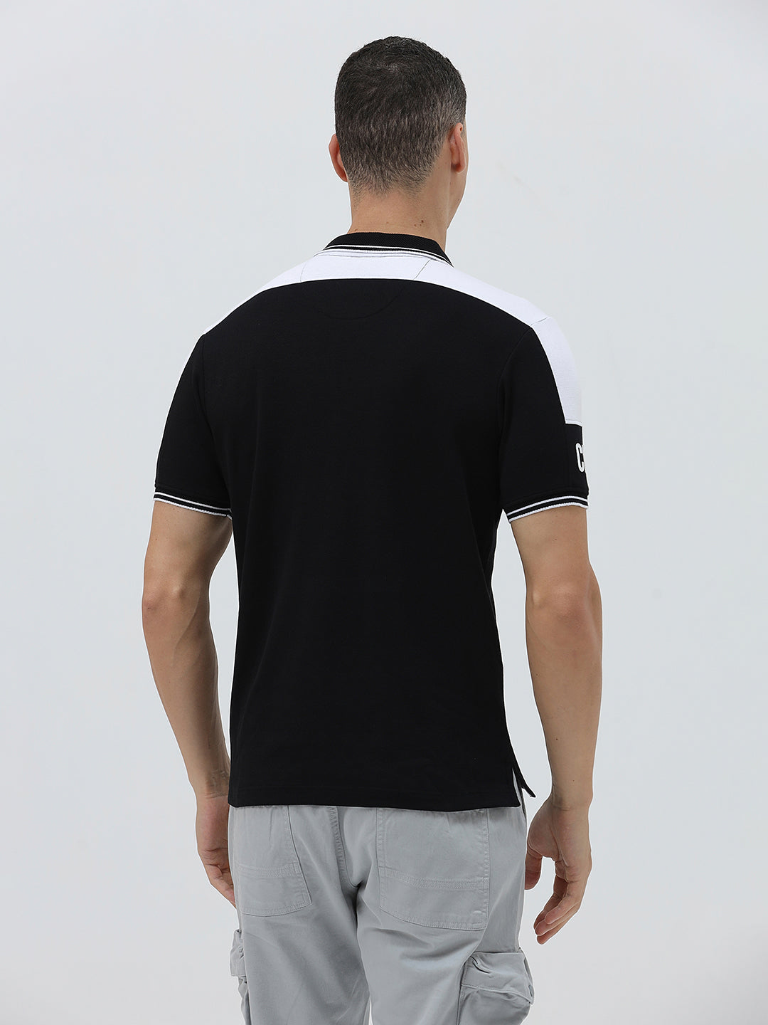 A man modeling a black short-sleeve polo shirt with white shoulder panels and white striped trim on the collar and sleeve cuffs, paired with light gray cargo pants against a plain light gray background.
