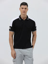 A man modeling a black short-sleeve polo shirt with white shoulder panels and white striped trim on the collar and sleeve cuffs, paired with light gray cargo pants against a plain light gray background.