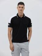 A man modeling a black short-sleeve polo shirt with white shoulder panels and white striped trim on the collar and sleeve cuffs, paired with light gray cargo pants against a plain light gray background.
