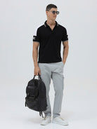 A man modeling a black short-sleeve polo shirt with white shoulder panels and white striped trim on the collar and sleeve cuffs, paired with light gray cargo pants against a plain light gray background.