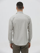 A man wearing a light gray long-sleeve button-down shirt with a small repeating geometric pattern, paired with olive green trousers, against a plain light gray background.