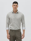 A man wearing a light gray long-sleeve button-down shirt with a small repeating geometric pattern, paired with olive green trousers, against a plain light gray background.