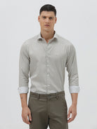 A man wearing a light gray long-sleeve button-down shirt with a small repeating geometric pattern, paired with olive green trousers, against a plain light gray background.