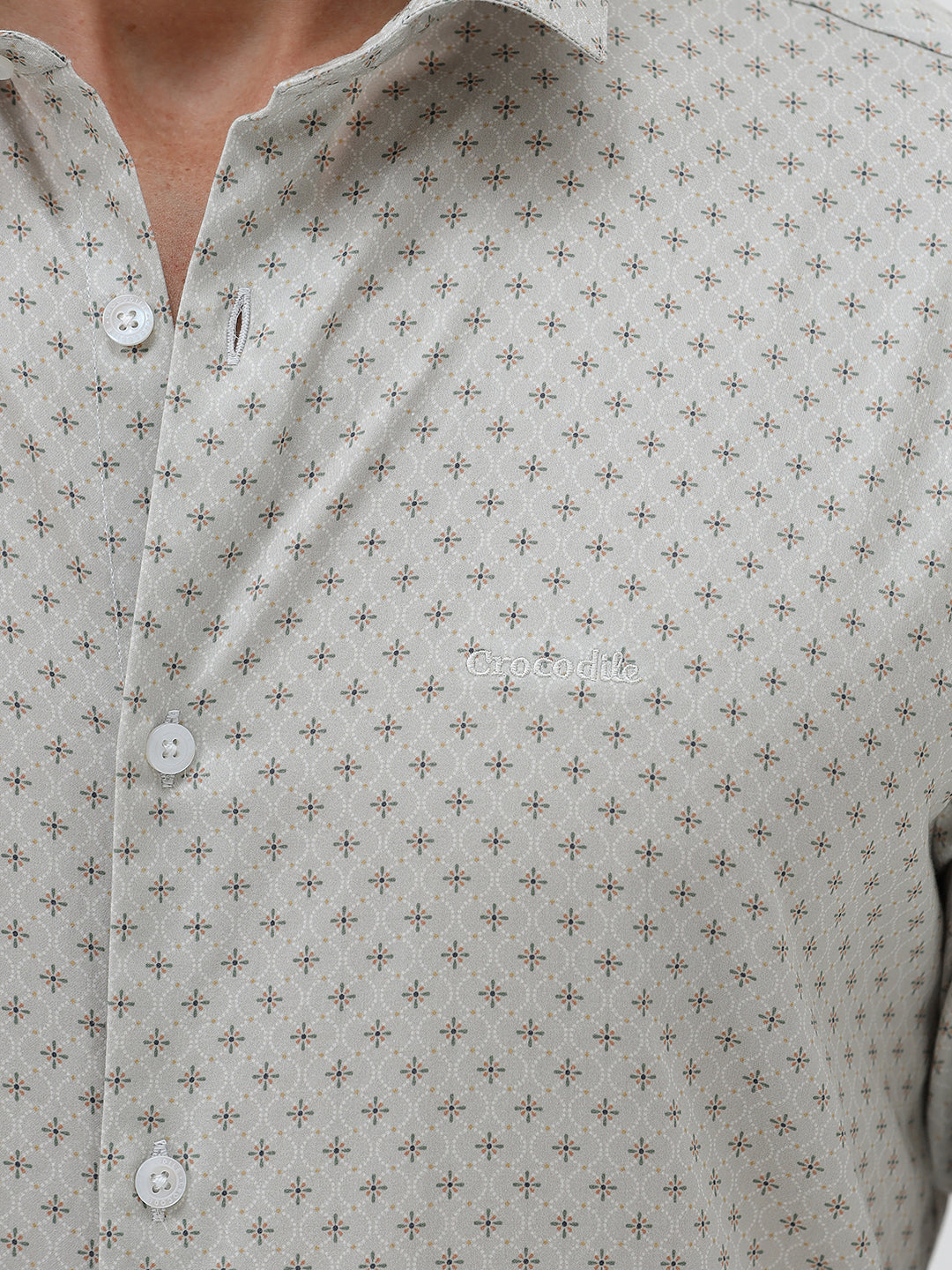 A man wearing a light gray long-sleeve button-down shirt with a small repeating geometric pattern, paired with olive green trousers, against a plain light gray background.