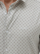 A man wearing a light gray long-sleeve button-down shirt with a small repeating geometric pattern, paired with olive green trousers, against a plain light gray background.