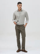 A man wearing a light gray long-sleeve button-down shirt with a small repeating geometric pattern, paired with olive green trousers, against a plain light gray background.