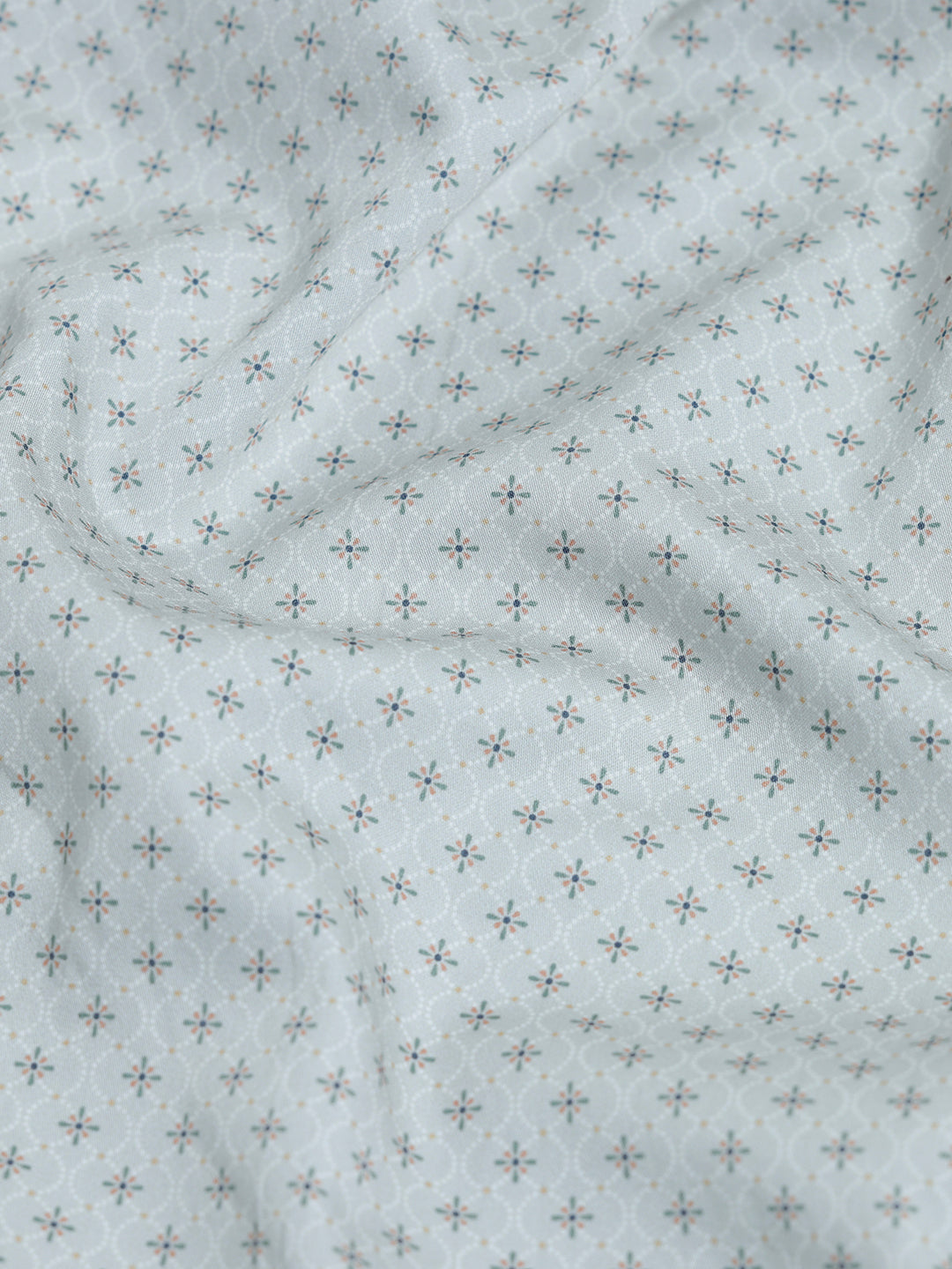 A man wearing a light gray long-sleeve button-down shirt with a small repeating geometric pattern, paired with olive green trousers, against a plain light gray background.