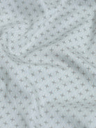 A man wearing a light gray long-sleeve button-down shirt with a small repeating geometric pattern, paired with olive green trousers, against a plain light gray background.