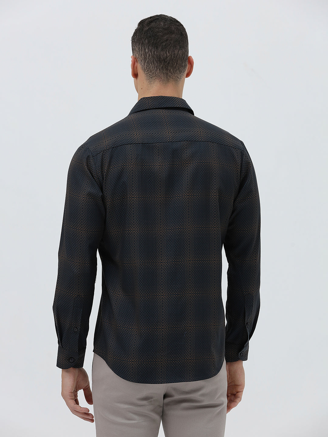A man wearing a dark charcoal gray long-sleeve button-down shirt with a subtle grid pattern, paired with light gray trousers, against a plain light gray background.