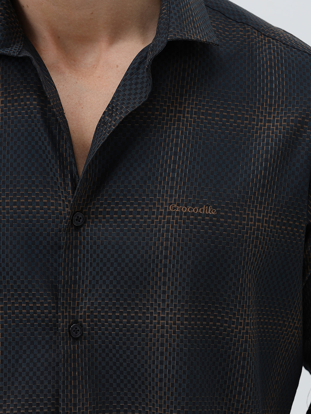 A man wearing a dark charcoal gray long-sleeve button-down shirt with a subtle grid pattern, paired with light gray trousers, against a plain light gray background.