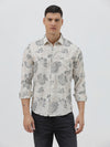 A man wearing a long-sleeve button-up shirt with a gray floral pattern on a cream-colored base, paired with dark gray trousers, against a plain light gray background.